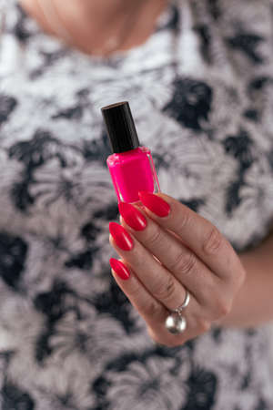 Female hand with long nails and a bottle bright neon pink red color nail polishの写真素材