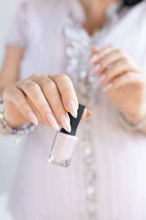 Woman hand with long nails manicure and light pink bottle with nail polish