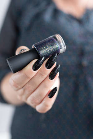 Female hand with long nails and black manicure holds a bottle of nail polish