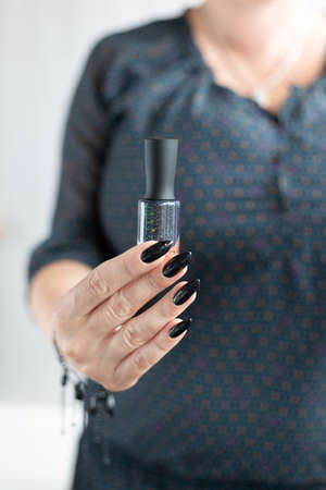 Female hand with long nails and black manicure holds a bottle of nail polishの写真素材