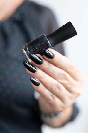Female hand with long nails and black manicure holds a bottle of nail polish