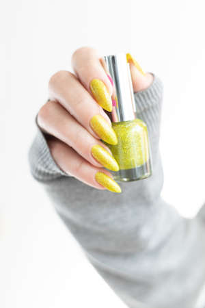 one female hand with long nails and a bottle of bright yellow green nail polish