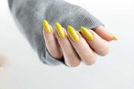 one female hand with long nails and a bottle of bright yellow green nail polishの写真素材