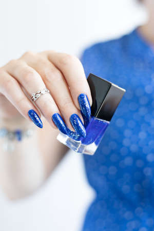 Woman's beautiful hand with long nails and blue manicure with bottles of nail polish