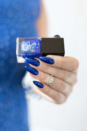 Woman's beautiful hand with long nails and blue manicure with bottles of nail polish
