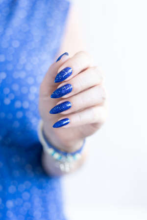Woman's beautiful hand with long nails and blue manicure with bottles of nail polishの写真素材