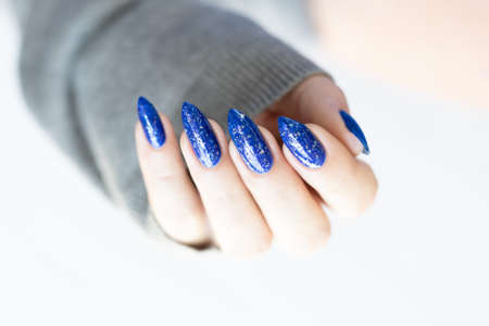 Woman's beautiful hand with long nails and blue manicure with bottles of nail polish