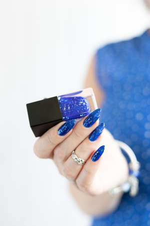 Woman's beautiful hand with long nails and blue manicure with bottles of nail polish
