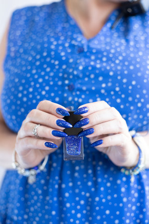 Woman's beautiful hand with long nails and blue manicure with bottles of nail polishの写真素材
