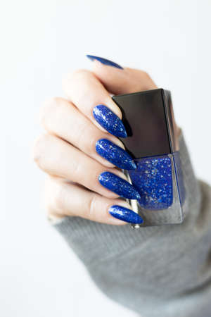 Woman's beautiful hand with long nails and blue manicure with bottles of nail polishの写真素材