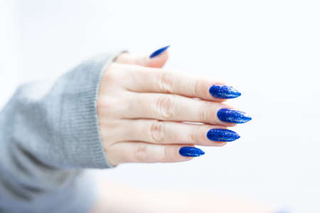 Woman's beautiful hand with long nails and blue manicure with bottles of nail polishの写真素材