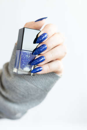 Woman's beautiful hand with long nails and blue manicure with bottles of nail polishの写真素材