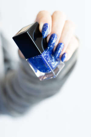 Woman's beautiful hand with long nails and blue manicure with bottles of nail polishの写真素材