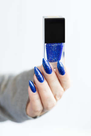 Woman's beautiful hand with long nails and blue manicure with bottles of nail polishの写真素材