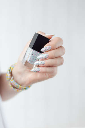 beautiful woman hands with long nails light white manicure and a bottle of nail polishの写真素材