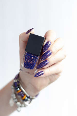 Female hand with long nails and purple lilac manicure holds a bottle of nail polish