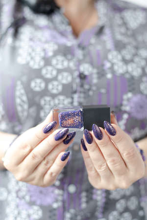 Female hand with long nails and purple lilac manicure holds a bottle of nail polish