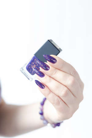 Female hand with long nails and purple lilac manicure holds a bottle of nail polish