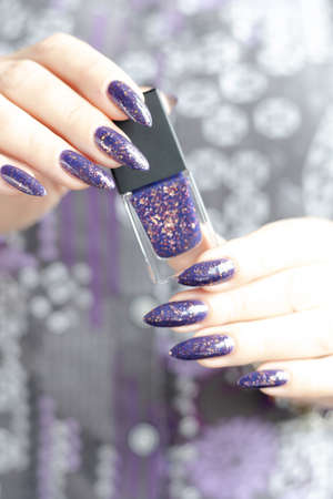 Female hand with long nails and purple lilac manicure holds a bottle of nail polish