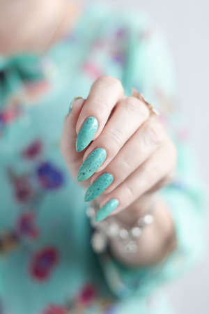 Female hand with long nails and green manicure with bottles of nail polishの写真素材