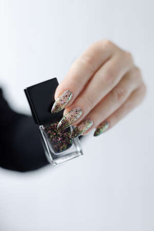 Woman's hands with long nails and white and black thermo manicure with bottles of nail polish
