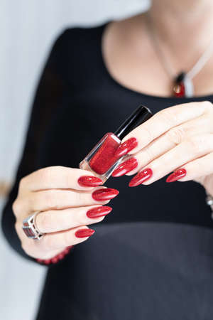 Female hand with long nails and a bottle with red nail polish