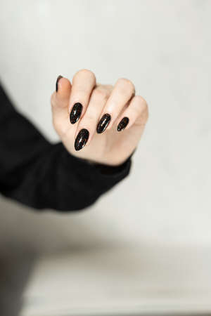 Female hand with long nails and black manicure with bottles of nail polishの写真素材