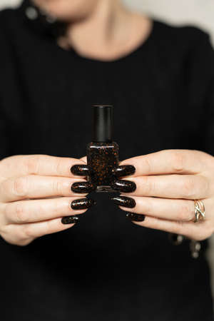 Female hand with long nails and black manicure with bottles of nail polishの写真素材