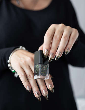 Woman's hands with long nails and white and black thermo manicure with bottles of nail polish