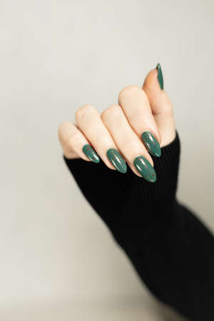 Female hand with long nails and green manicure with bottles of nail polishの写真素材