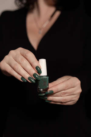 Female hand with long nails and green manicure with bottles of nail polishの写真素材