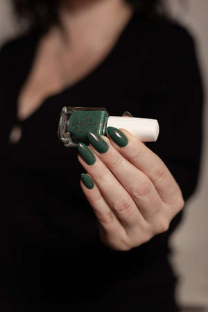 Female hand with long nails and green manicure with bottles of nail polishの写真素材