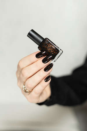 Female hand with long nails and black manicure with bottles of nail polish