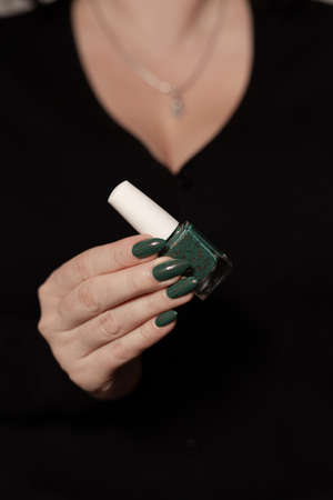Female hand with long nails and green manicure with bottles of nail polishの写真素材