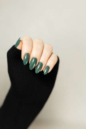 Female hand with long nails and green manicure with bottles of nail polishの写真素材