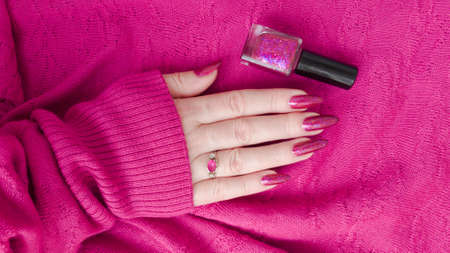 Female hand with long nails and a bottle of bright pink fuchsia neon nail polishの写真素材