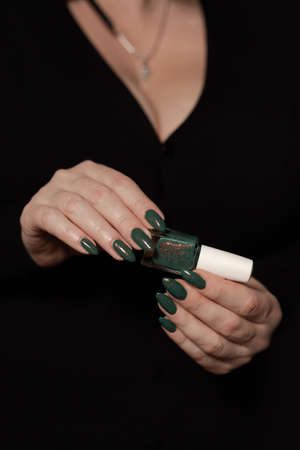 Female hand with long nails and green manicure with bottles of nail polish