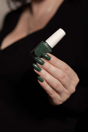 Female hand with long nails and green manicure with bottles of nail polishの写真素材