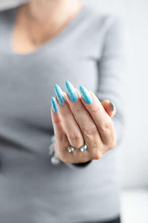 Female hand with long nails and light blue manicure with bottles of nail polishの写真素材