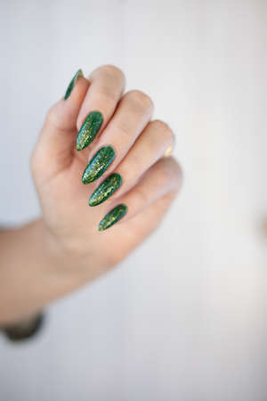 Female hand with long nails and green manicure with bottles of nail polishの写真素材