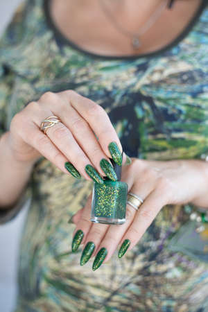 Female hand with long nails and green manicure with bottles of nail polish