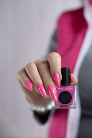 Female hand with long nails and a bottle of bright pink fuchsia neon nail polishの写真素材