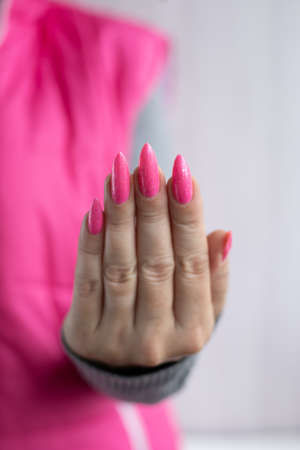 Female hand with long nails and a bottle of bright pink fuchsia neon nail polishの写真素材