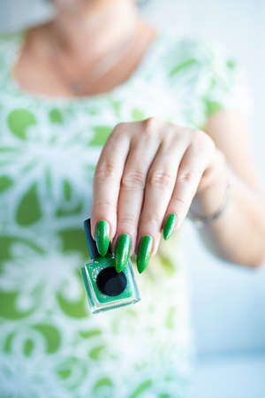 Female hand with long nails and green manicure with bottles of nail polishの写真素材