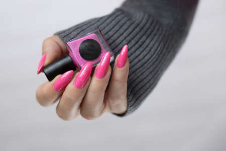 Female hand with long nails and a bottle of bright pink fuchsia neon nail polishの写真素材