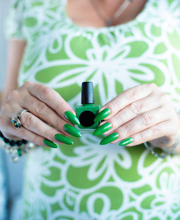 Female hand with long nails and bright green manicure with bottles of nail polish