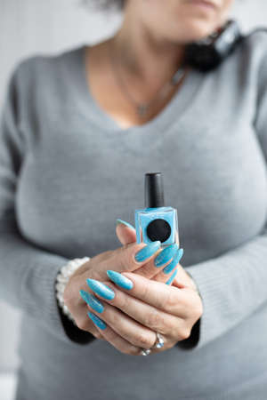 Female hand with long nails and light blue manicure with bottles of nail polishの写真素材