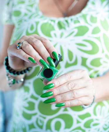 Female hand with long nails and green manicure with bottles of nail polishの写真素材