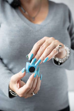 Woman's beautiful hand with long nails and light blue manicure with bottles of nail polishの写真素材