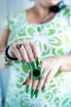 Female hand with long nails and bright green manicure with bottles of nail polishの写真素材